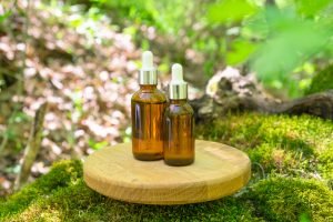 Natural skincare products in glass bottles displayed on wooden podium in lush forest setting surrounded by greenery