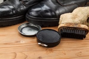 Shoe polish with brush, cloth and worn boots on wooden platform.