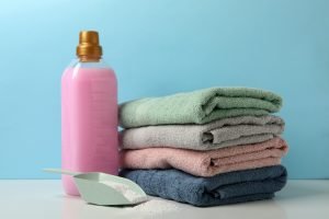 Detergent, scoop with powder and towels on white table against blue background